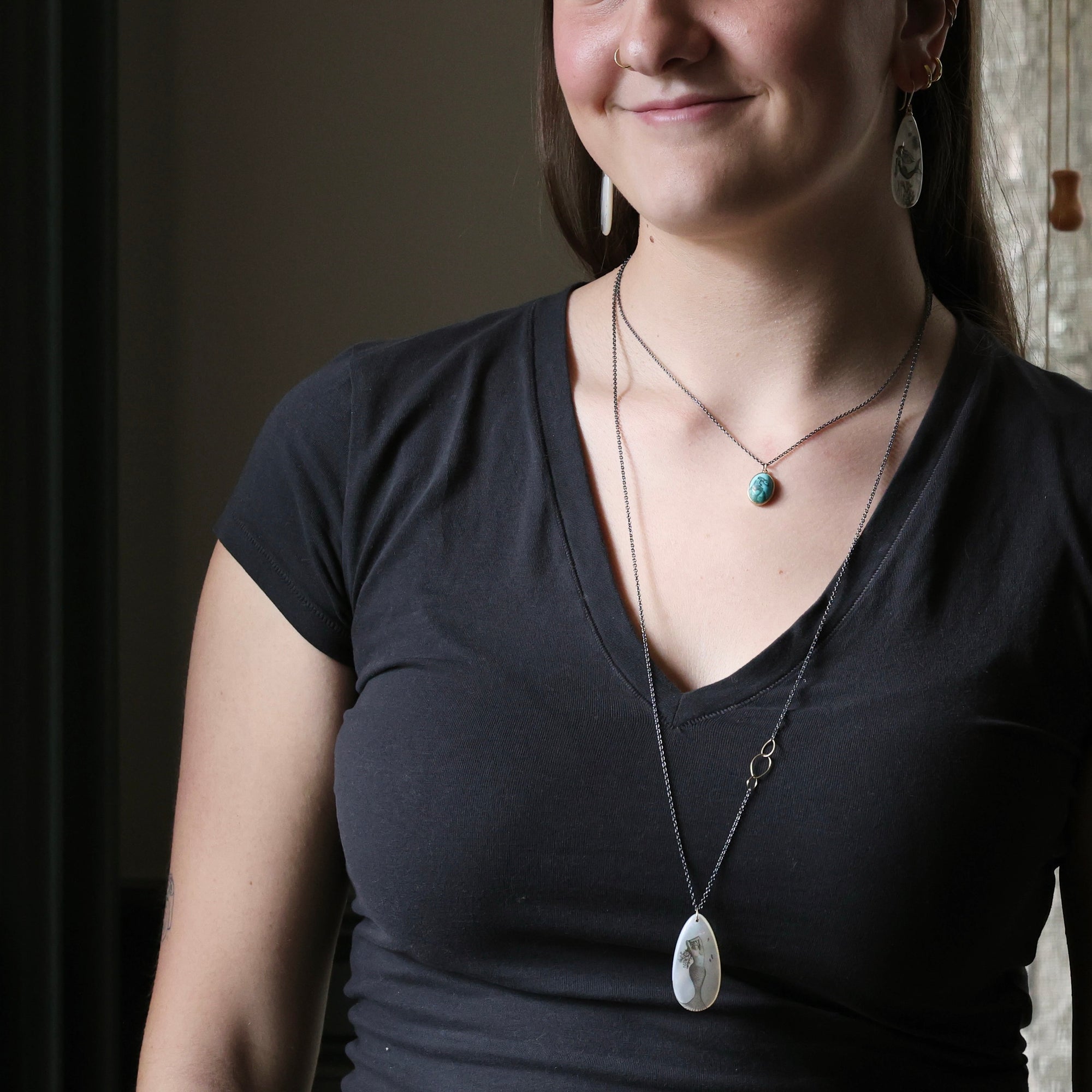 Woman wearing a black top and a necklace with a pendant indoors.
