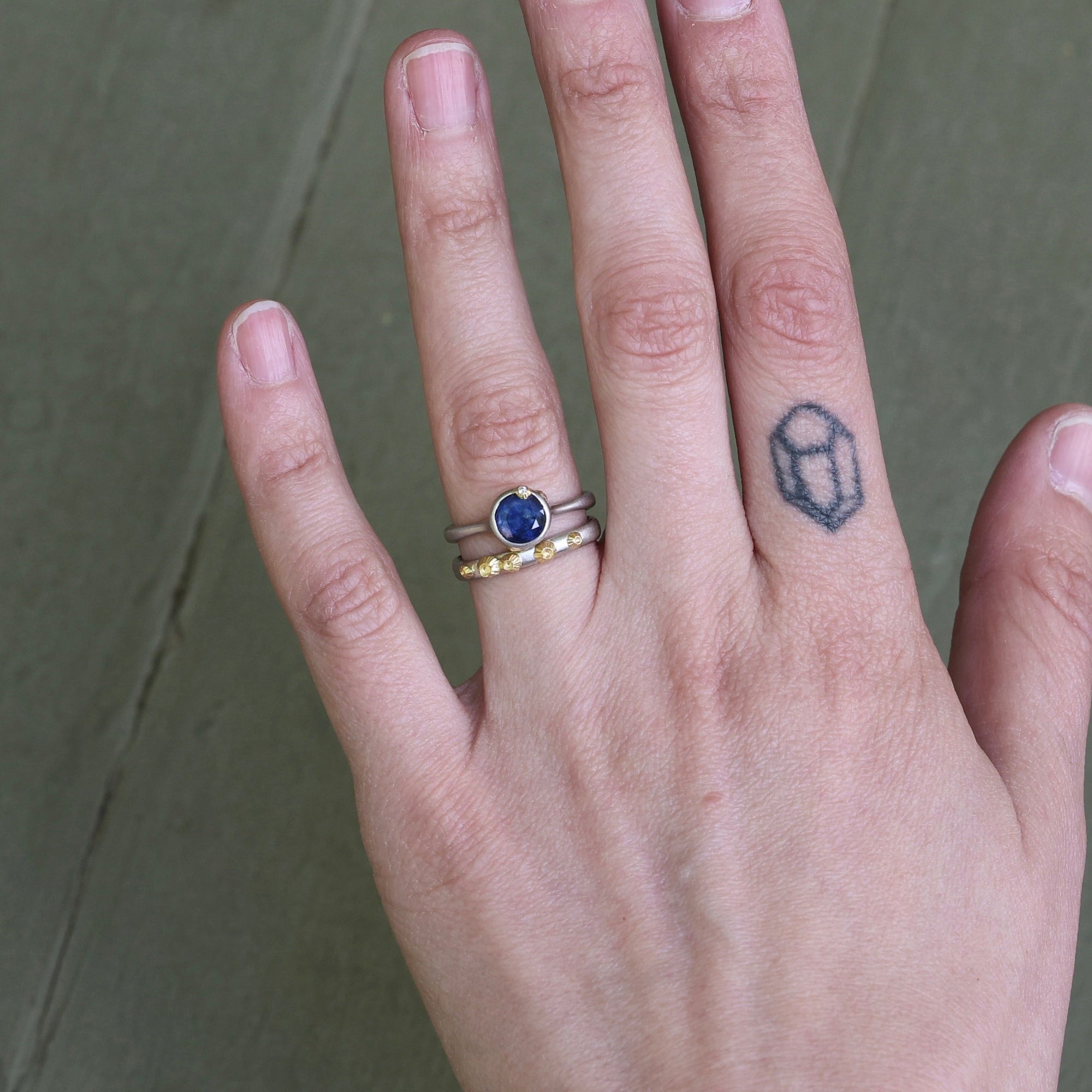 Hand wearing blue gemstone ring with gold barnacles and wedding band