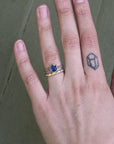 Hand wearing blue gemstone ring with gold barnacles and wedding band
