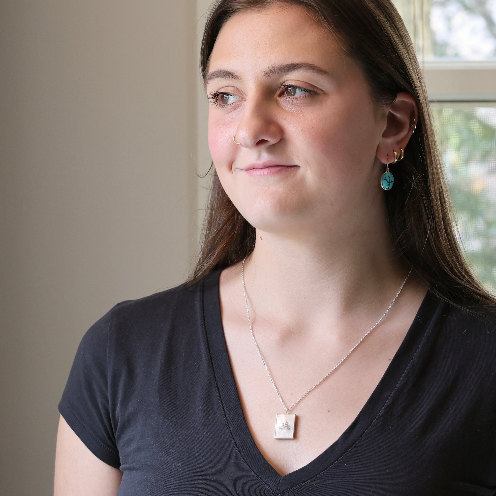 Woman wearing a black shirt with a necklace and earrings indoors.