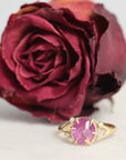 Gold ring with a pink gemstone next to a red rose on a light background