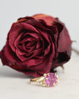 Gold ring with a pink gemstone next to a dried red rose on a light background