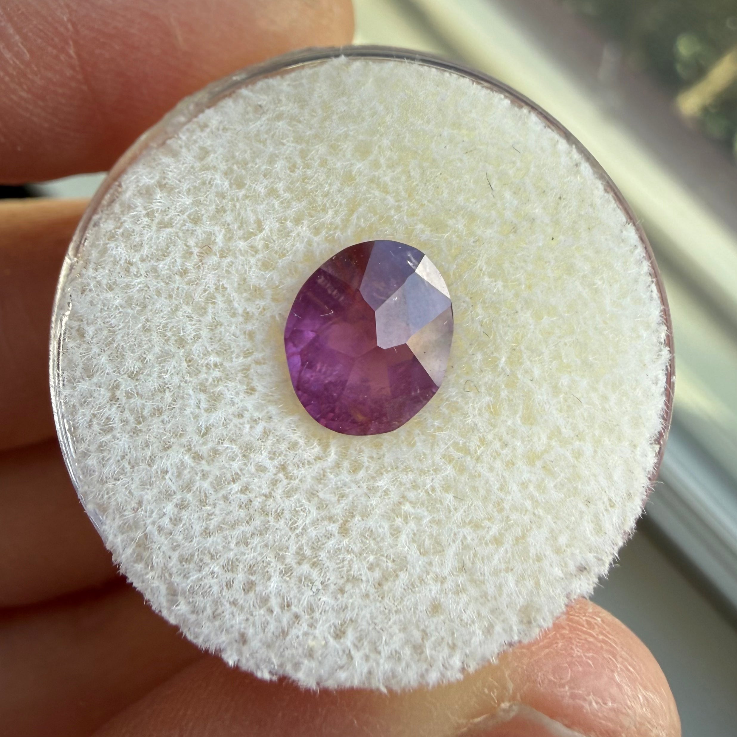 Round purple gemstone on a textured white background held by fingers.