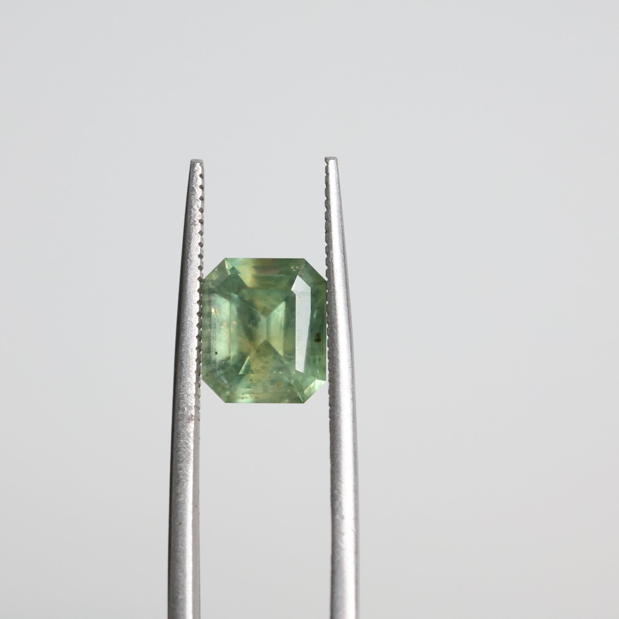 Tweezers holding green emerald cut Montana sapphire