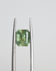 Tweezers holding green emerald cut Montana sapphire