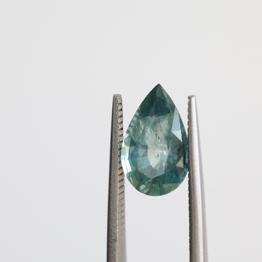Green pear shaped sapphire held in tweezers