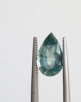 Green pear shaped sapphire held in tweezers