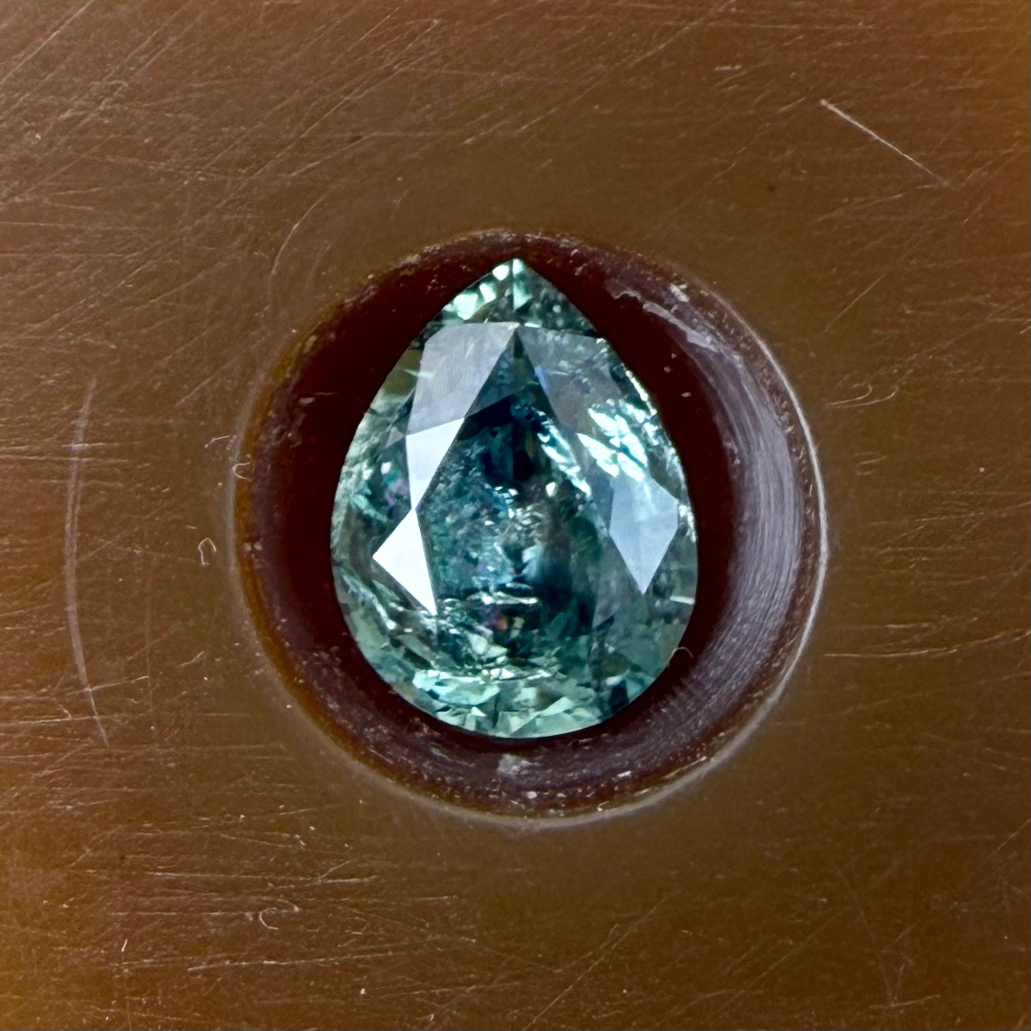 Teal gemstone in a brown setting on a brown background