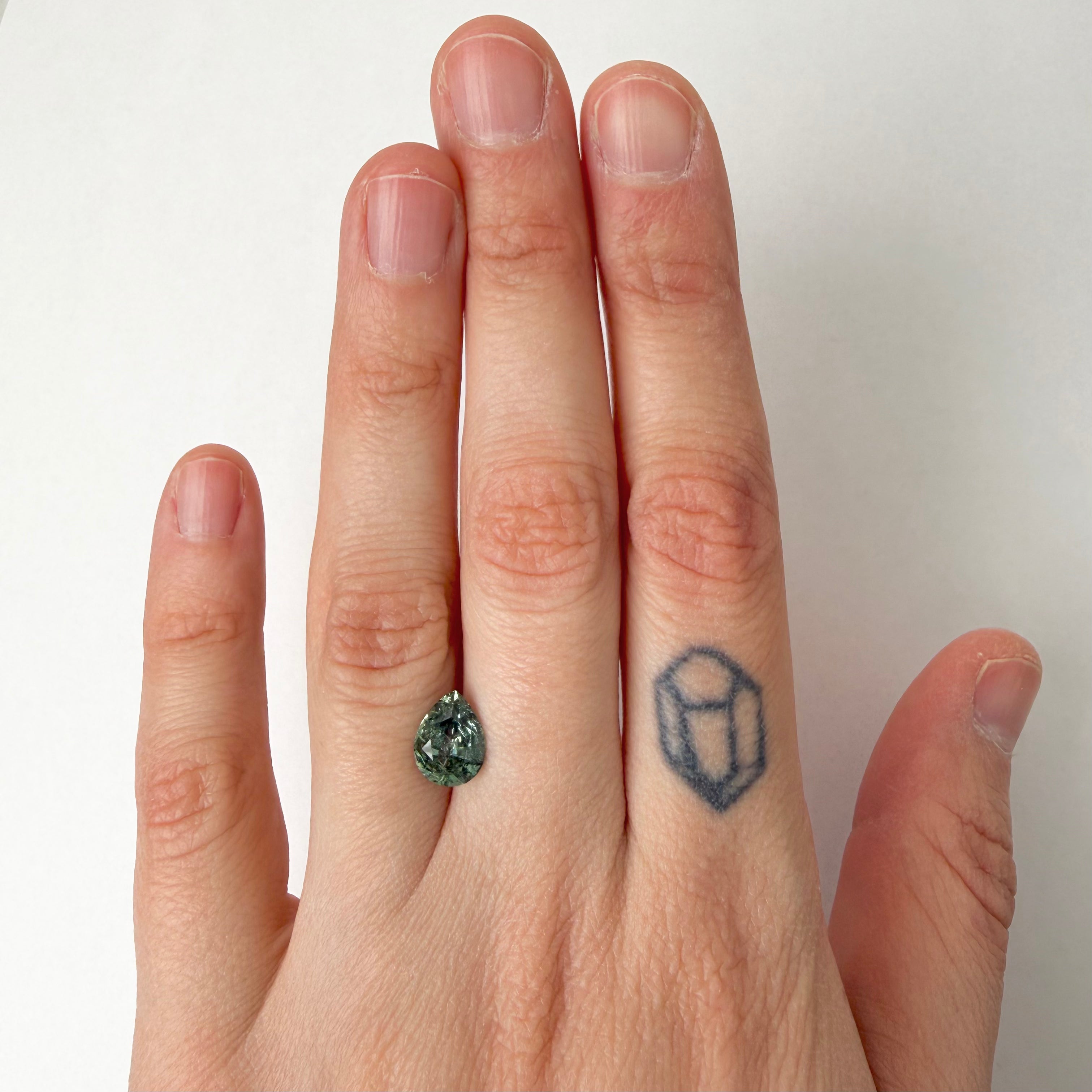 Hand wearing a ring with a green gemstone on a plain background
