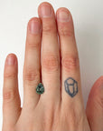 Hand wearing a ring with a green gemstone on a plain background