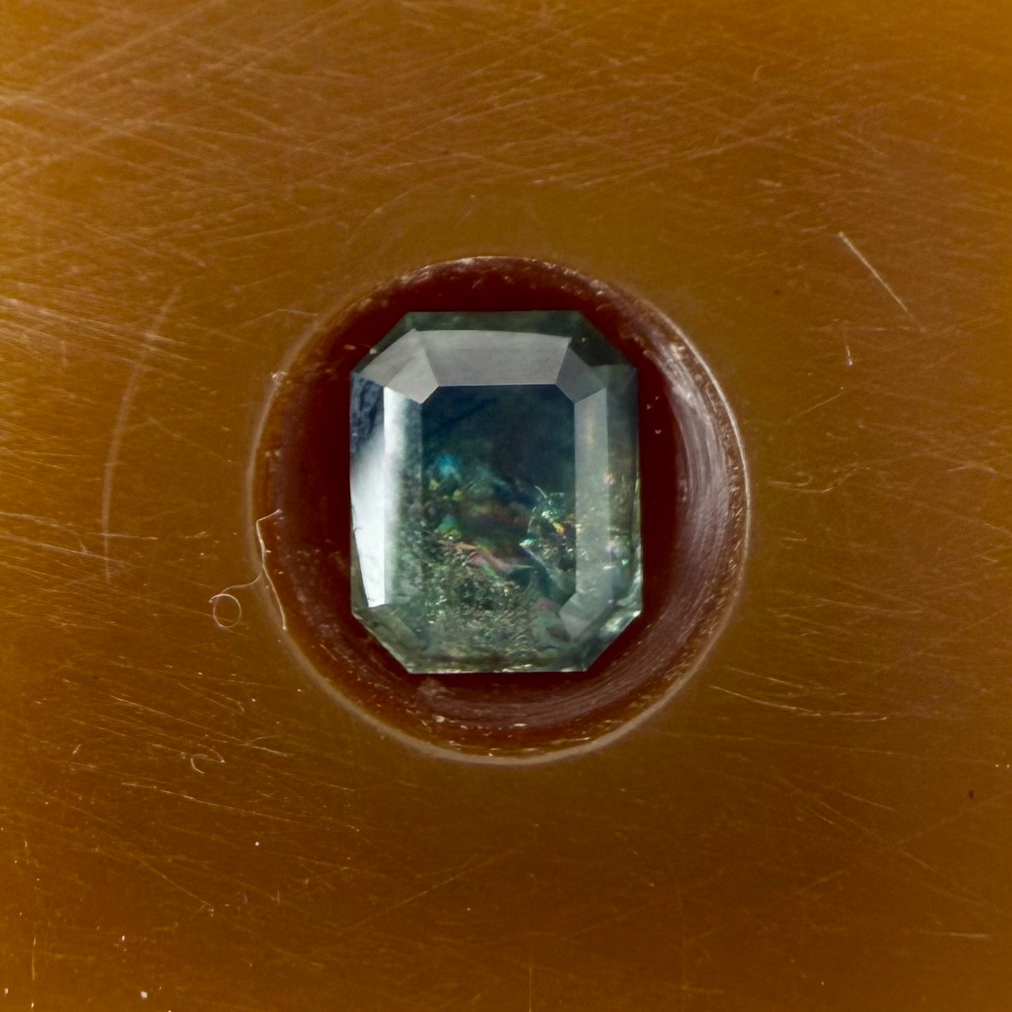 Faceted gemstone in a brown setting on a brown background
