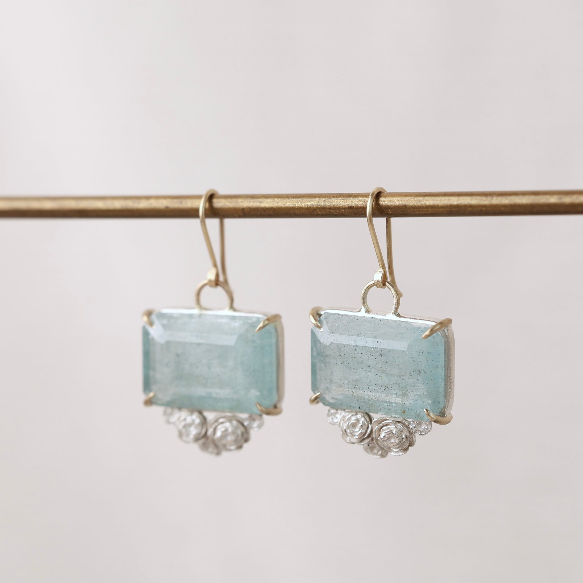 Pair of earrings with rectangular light blue stones on a thin rod against a light background