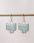 Pair of earrings with rectangular light blue stones on a thin rod against a light background