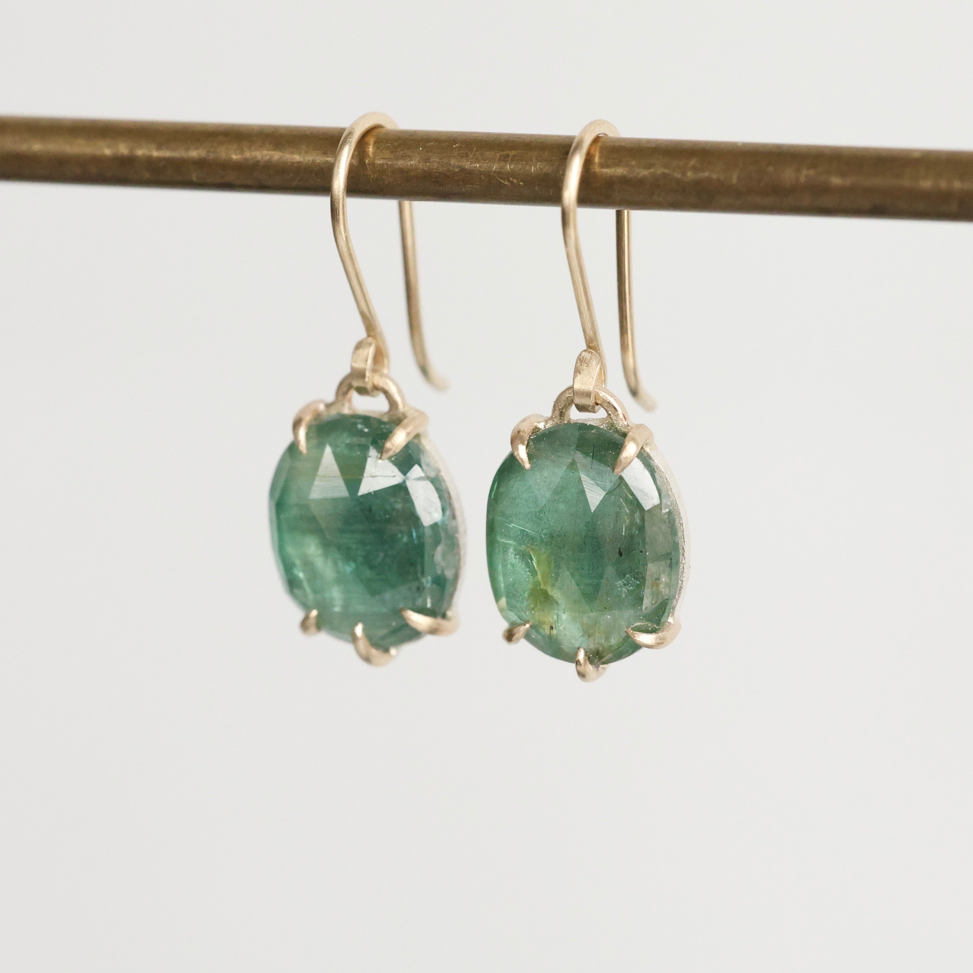 Green gemstone earrings on a thin rod against a light gray background