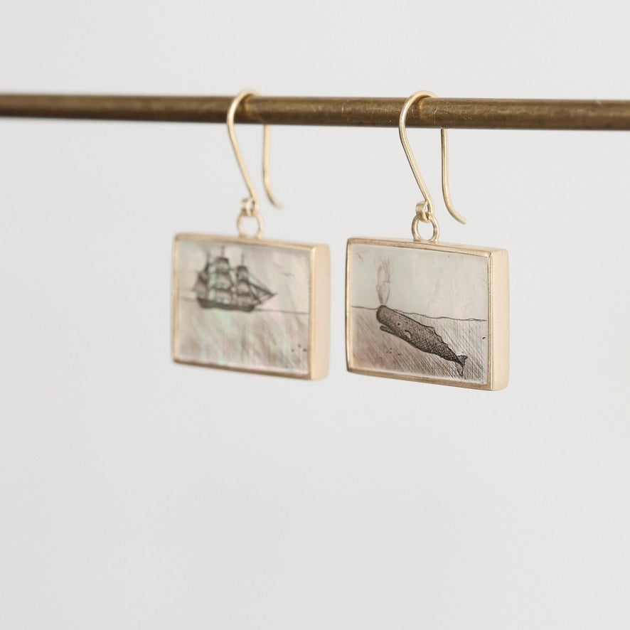 Pair of earrings with ship and whale design on a white background