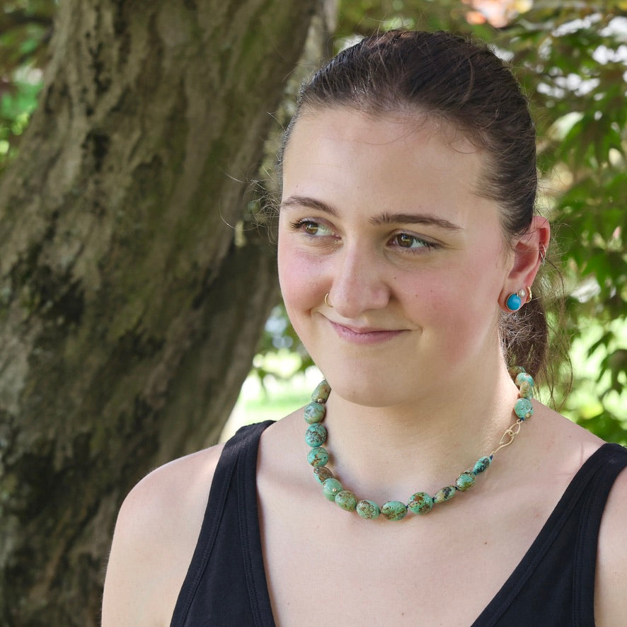 Woman wearing a green beaded necklace outdoors with trees in the background