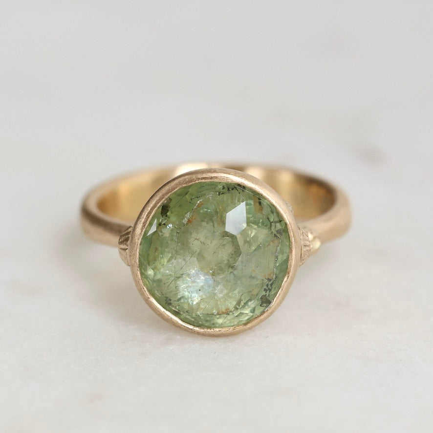 Gold ring with a green gemstone on a light gray background