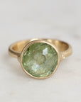 Gold ring with a green gemstone on a light gray background