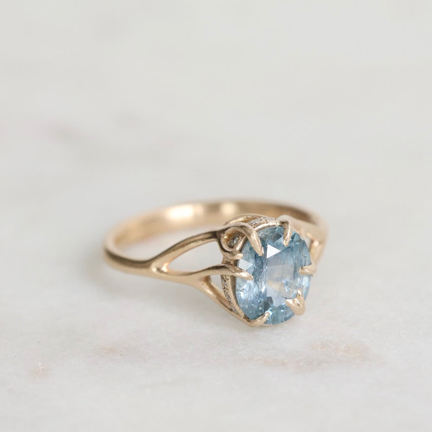 Gold ring with a blue gemstone on a light gray background