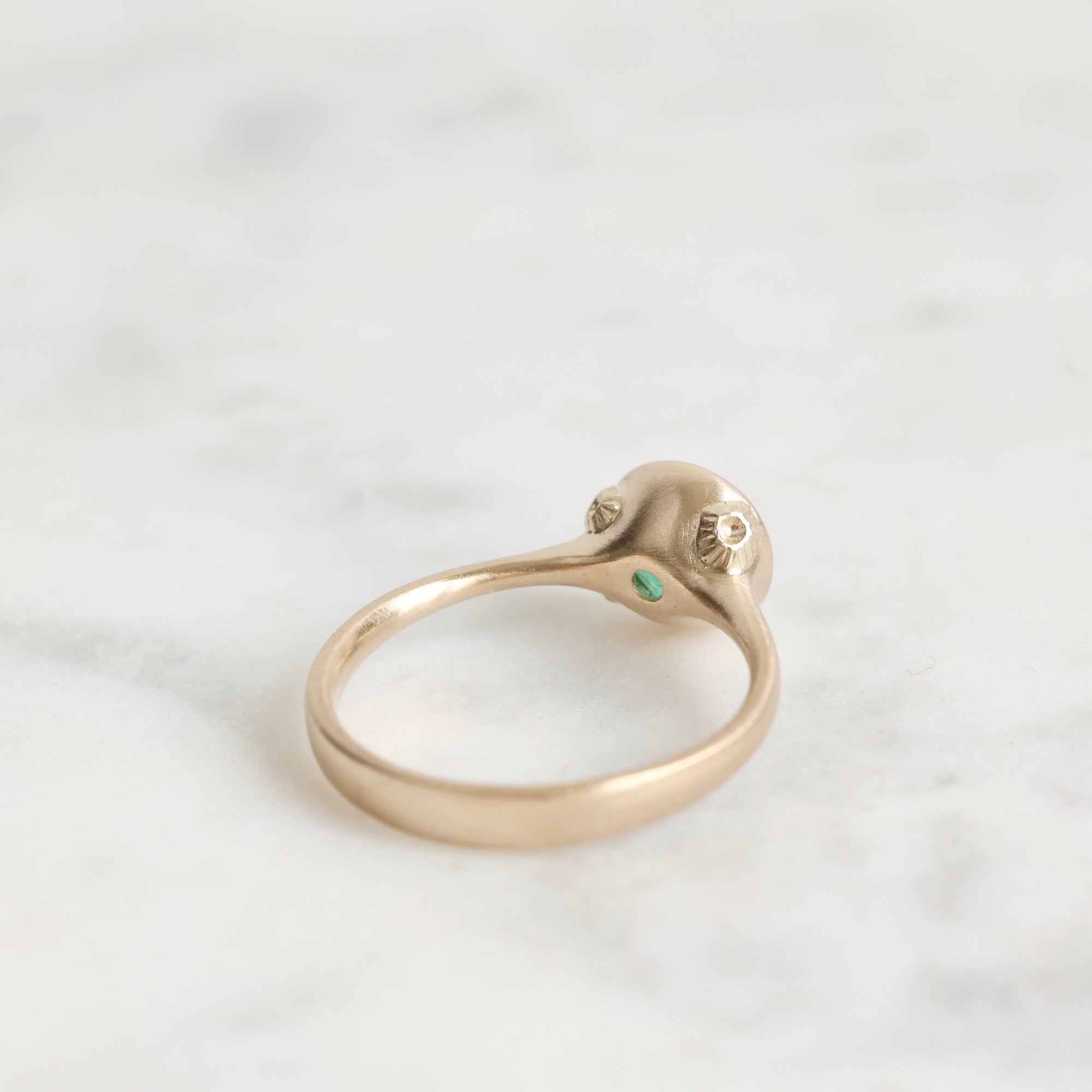 Gold ring with a small green gemstone on a light gray background