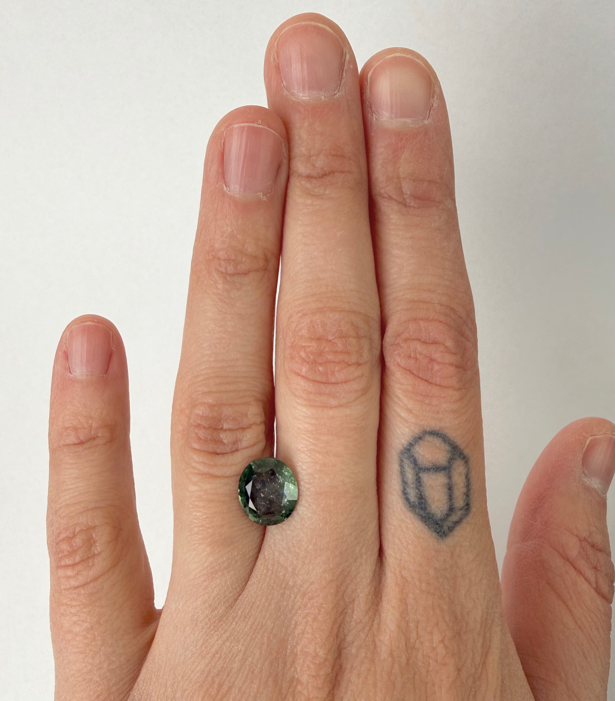 Green gemstone on hand with tattoo
