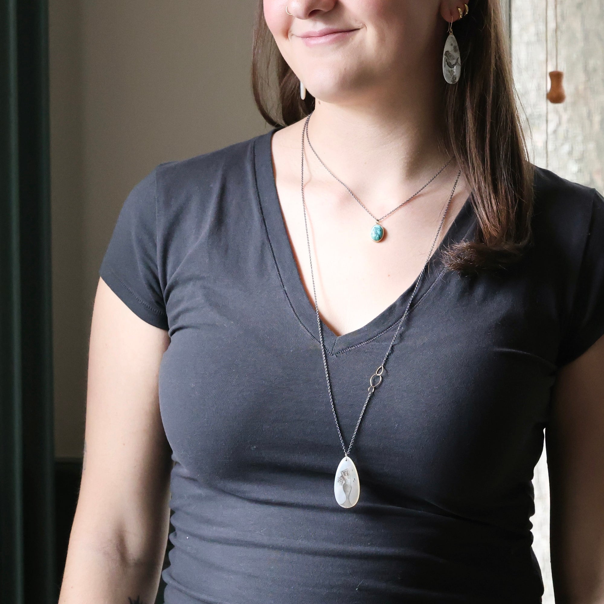 Woman wearing a dark gray shirt with necklaces and earrings indoors.