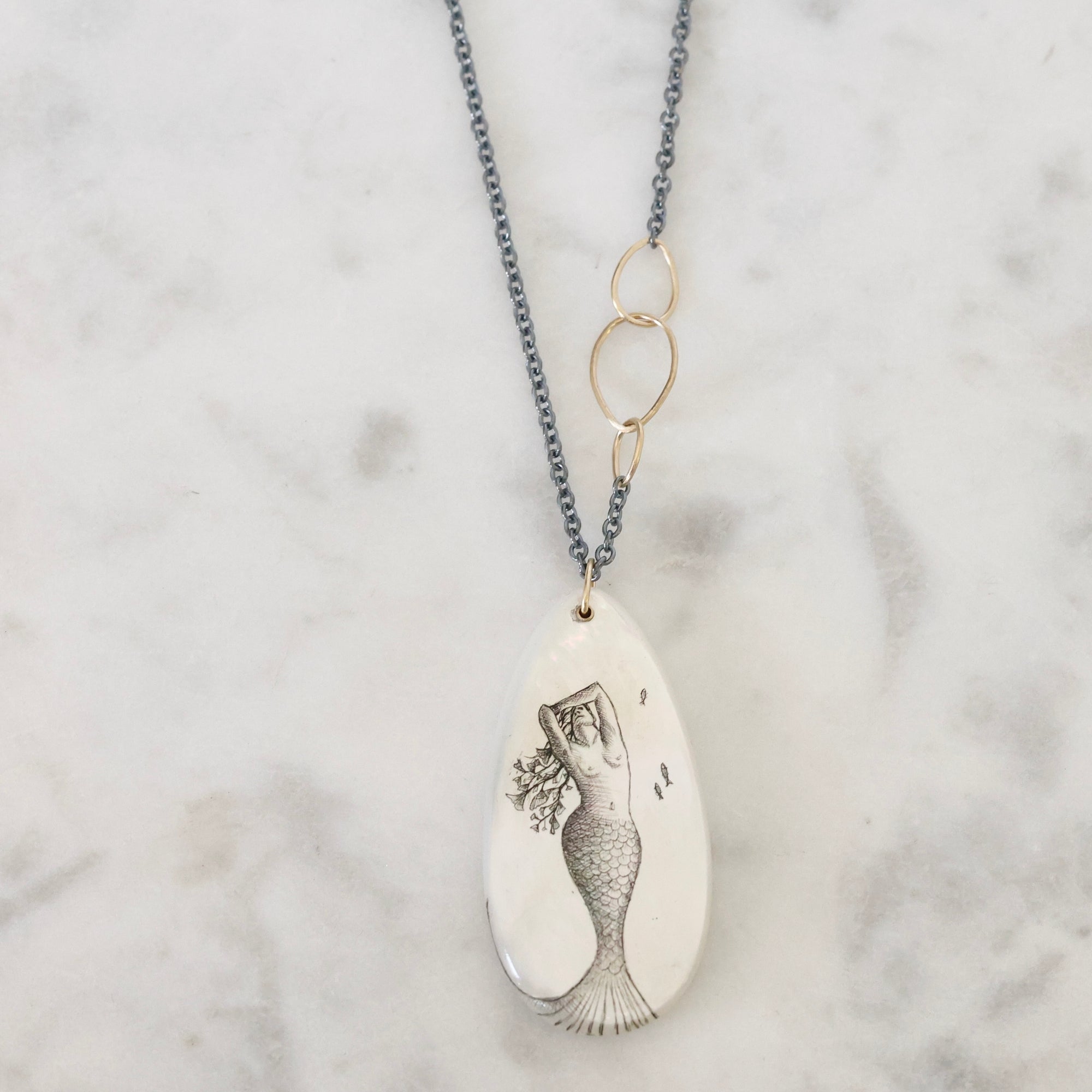 Necklace with a mermaid pendant on a marble surface