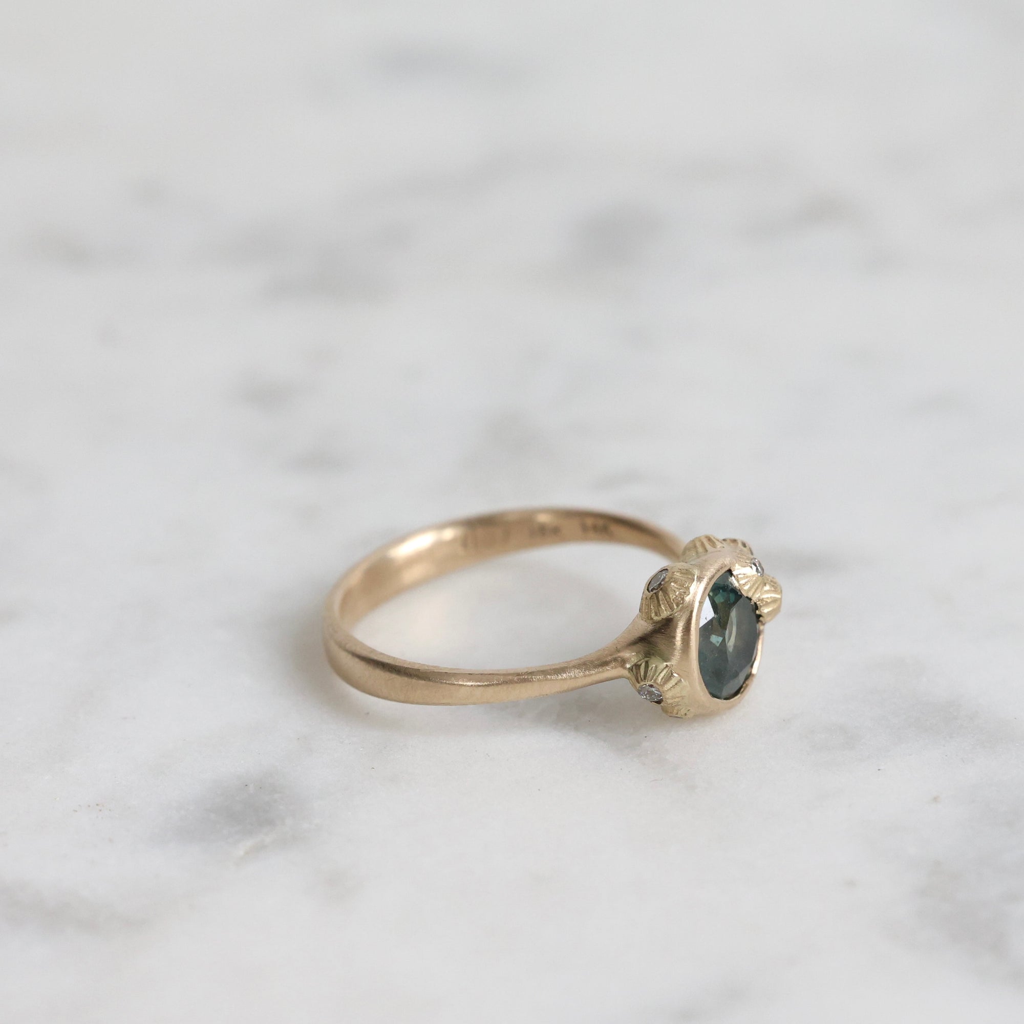 Gold ring with a dark gemstone on a marble surface
