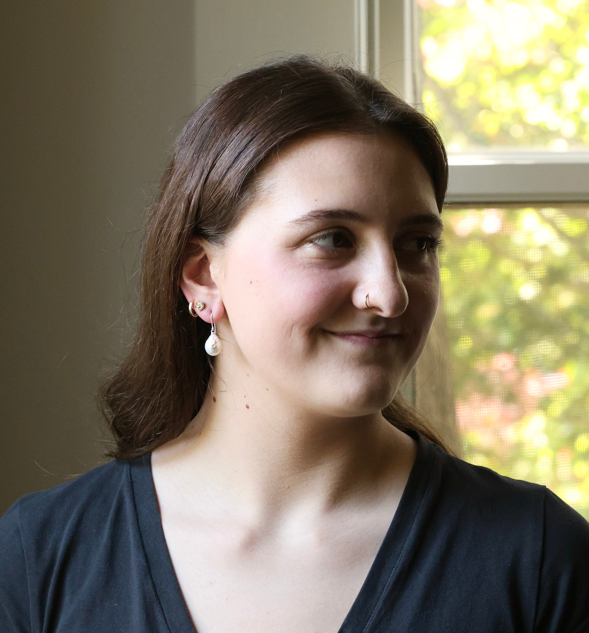 Woman with a slight smile in front of a window with greenery outside