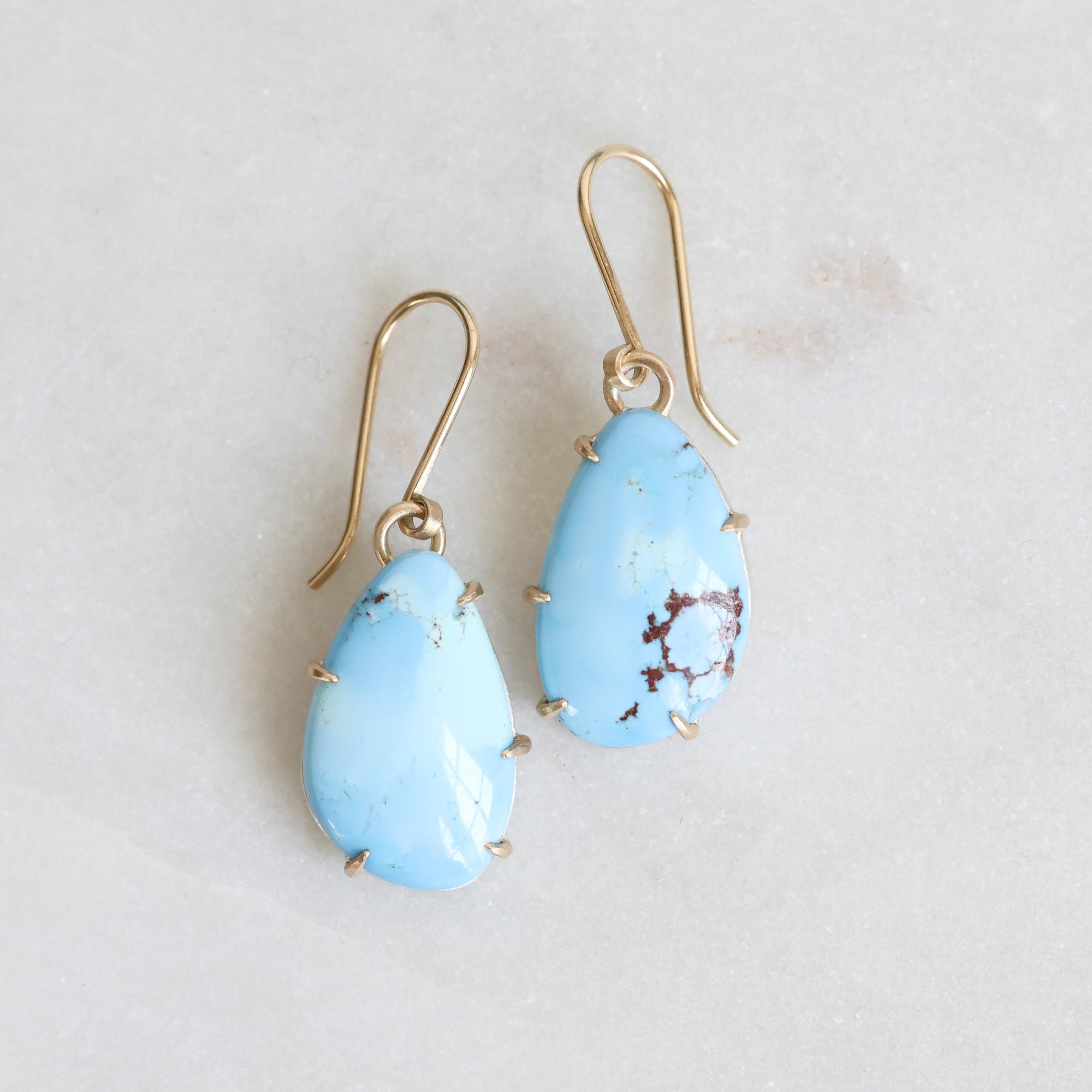 Pair of blue teardrop earrings on a gold earring stand against a light gray background