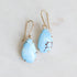 Pair of blue teardrop earrings on a gold earring stand against a light gray background