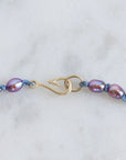 Necklace with purple beads and a gold clasp on a light gray background