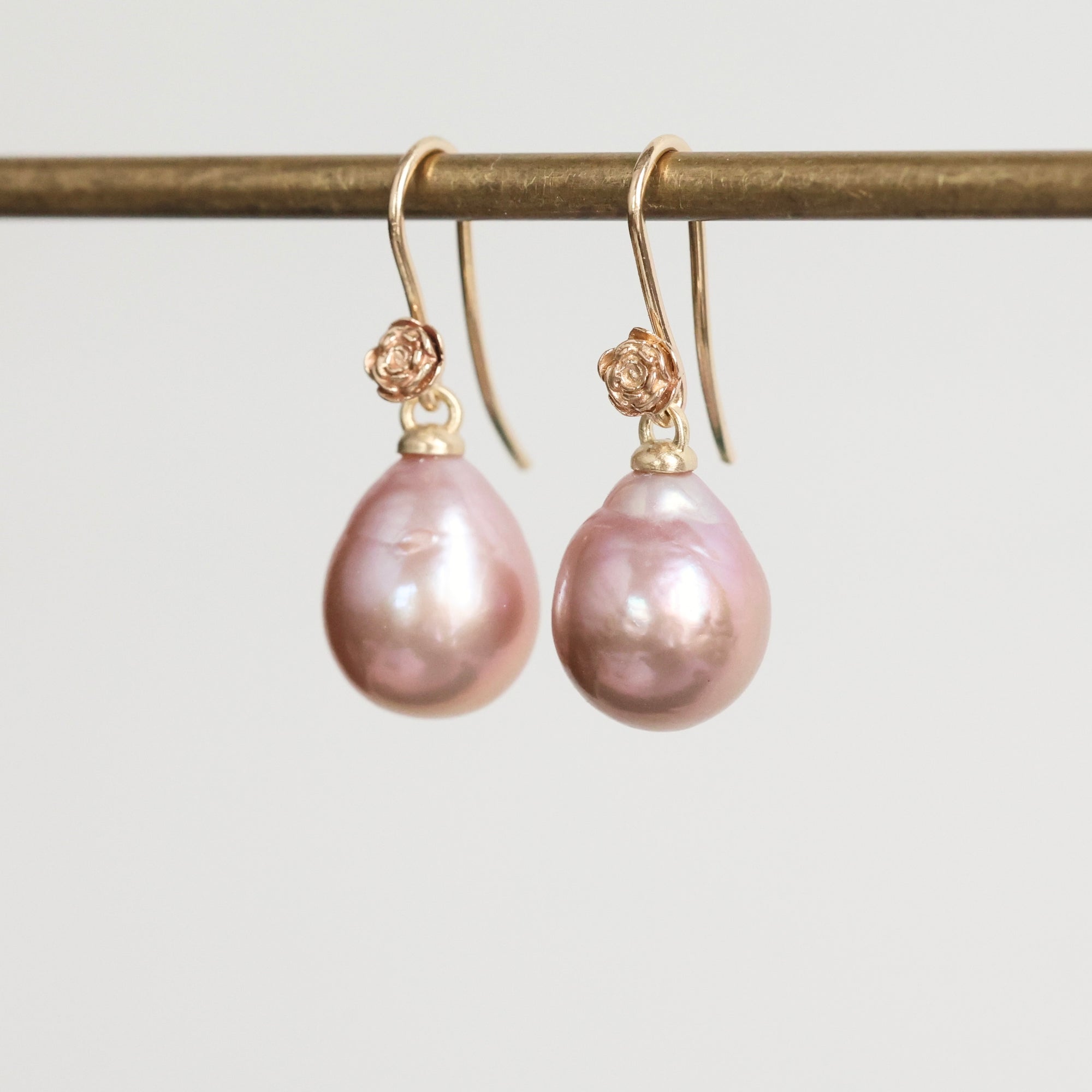 Pair of pink pearl earrings on a gold hook against a light gray background