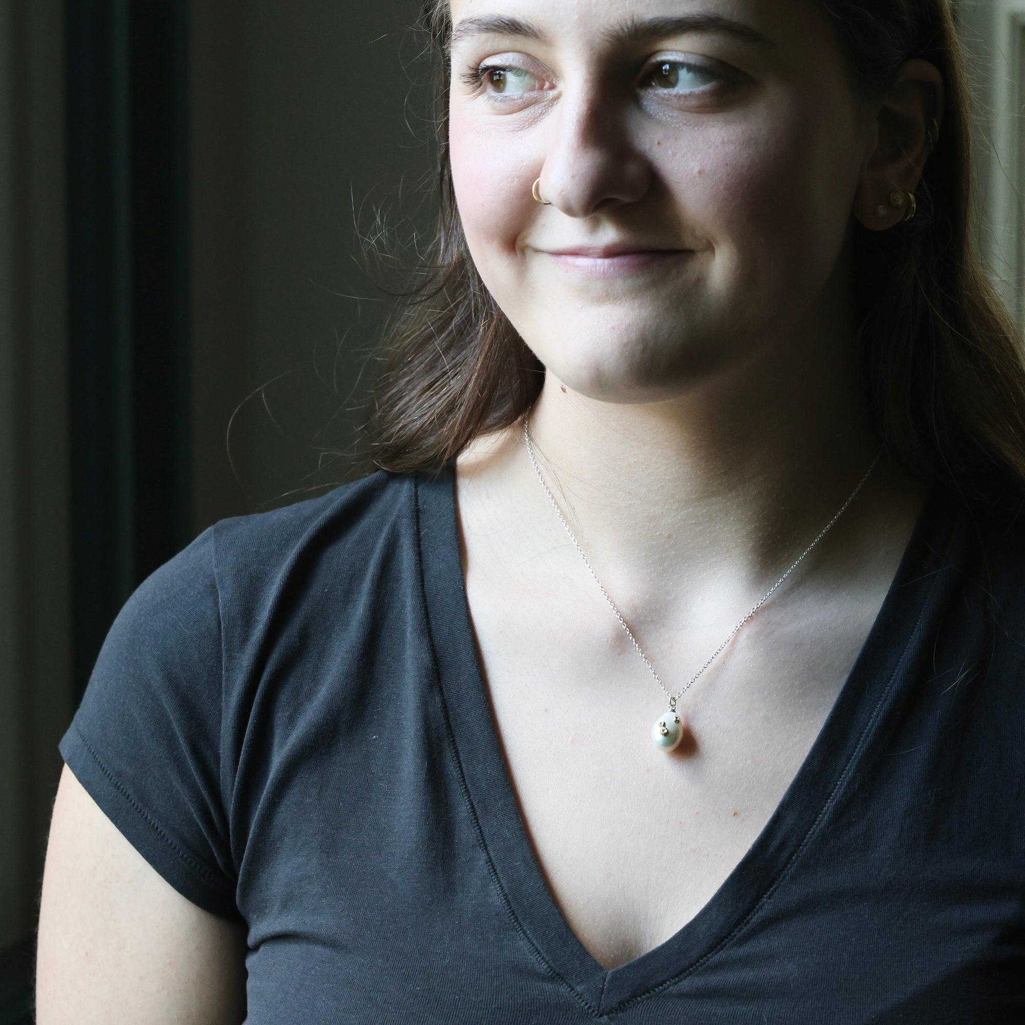 Woman wearing a necklace with a pendant against a dark background