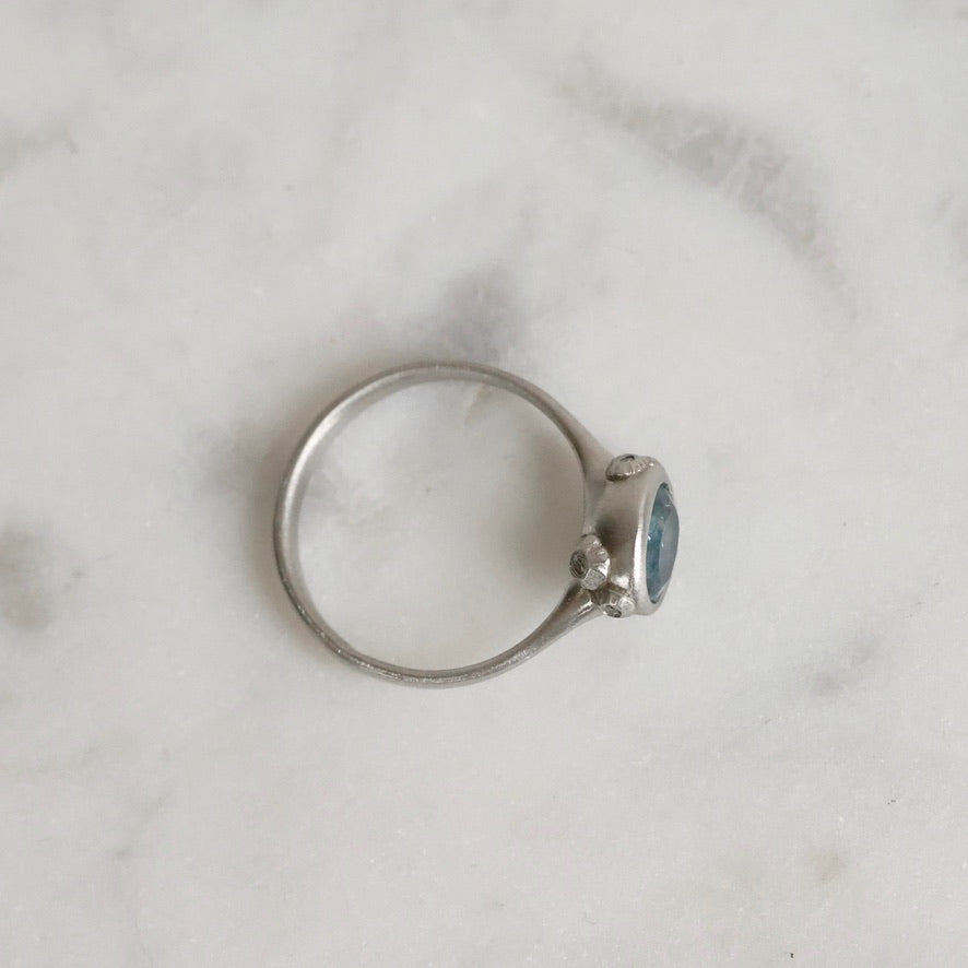 Silver ring with a blue gemstone on a marble surface