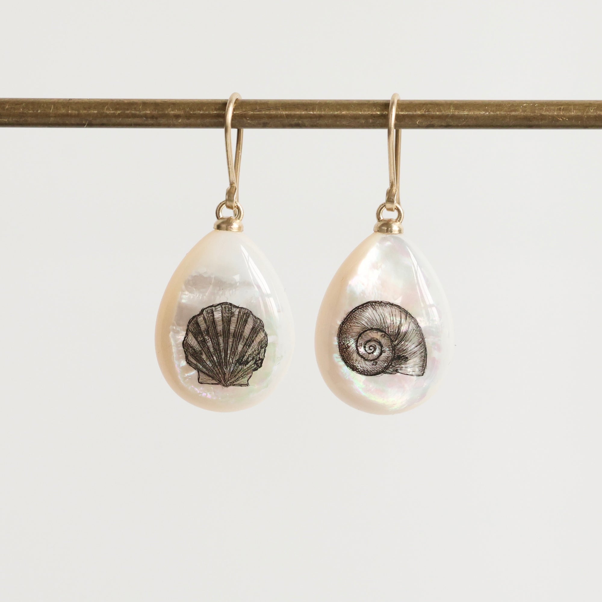 Teardrop-shaped earrings with shell designs on a white background