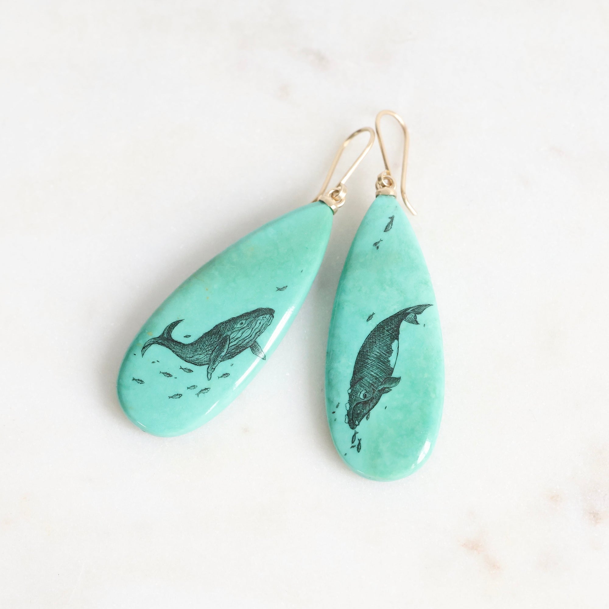Teal earrings with whale design on a white background