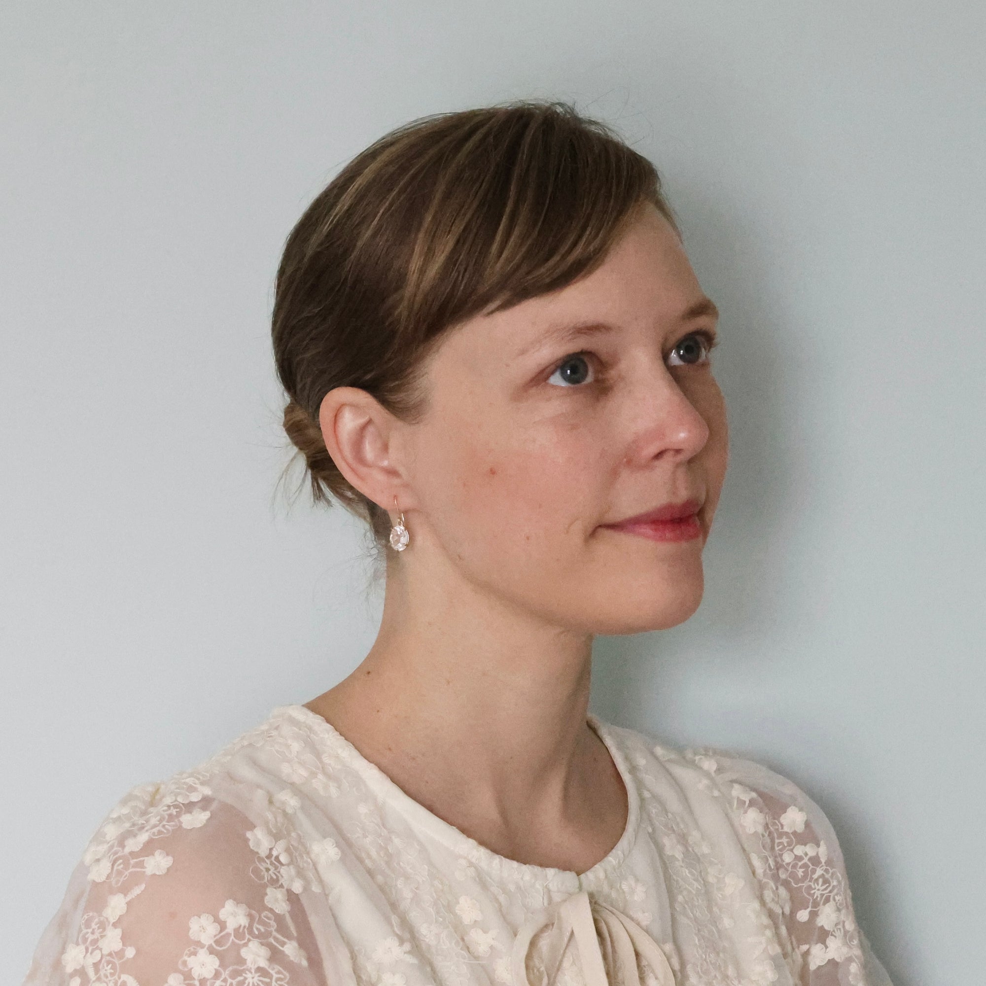 Woman wearing a white lace top against a plain background with drop herkimer quartz earrings