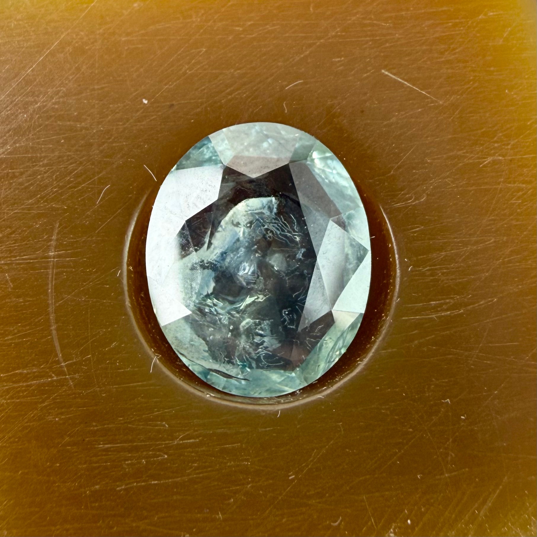 Greenish-blue oval gemstone in a brown setting on a textured brown background