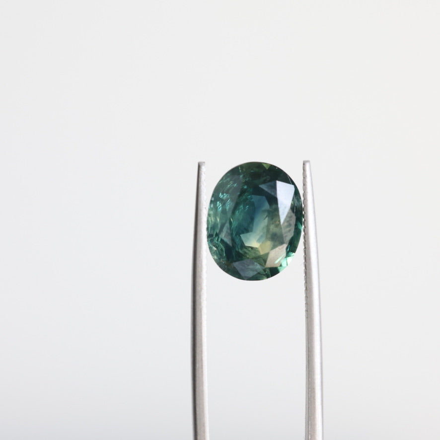 Green sapphire with inclusions held in tweezers