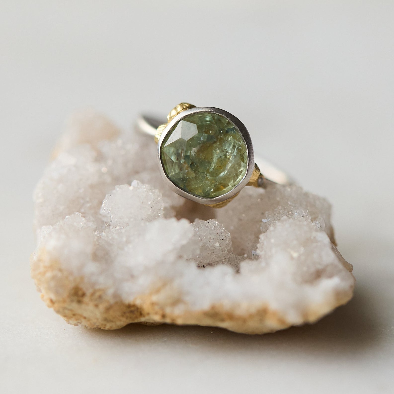 Ring with a green stone on a piece of crystal rock against a light background