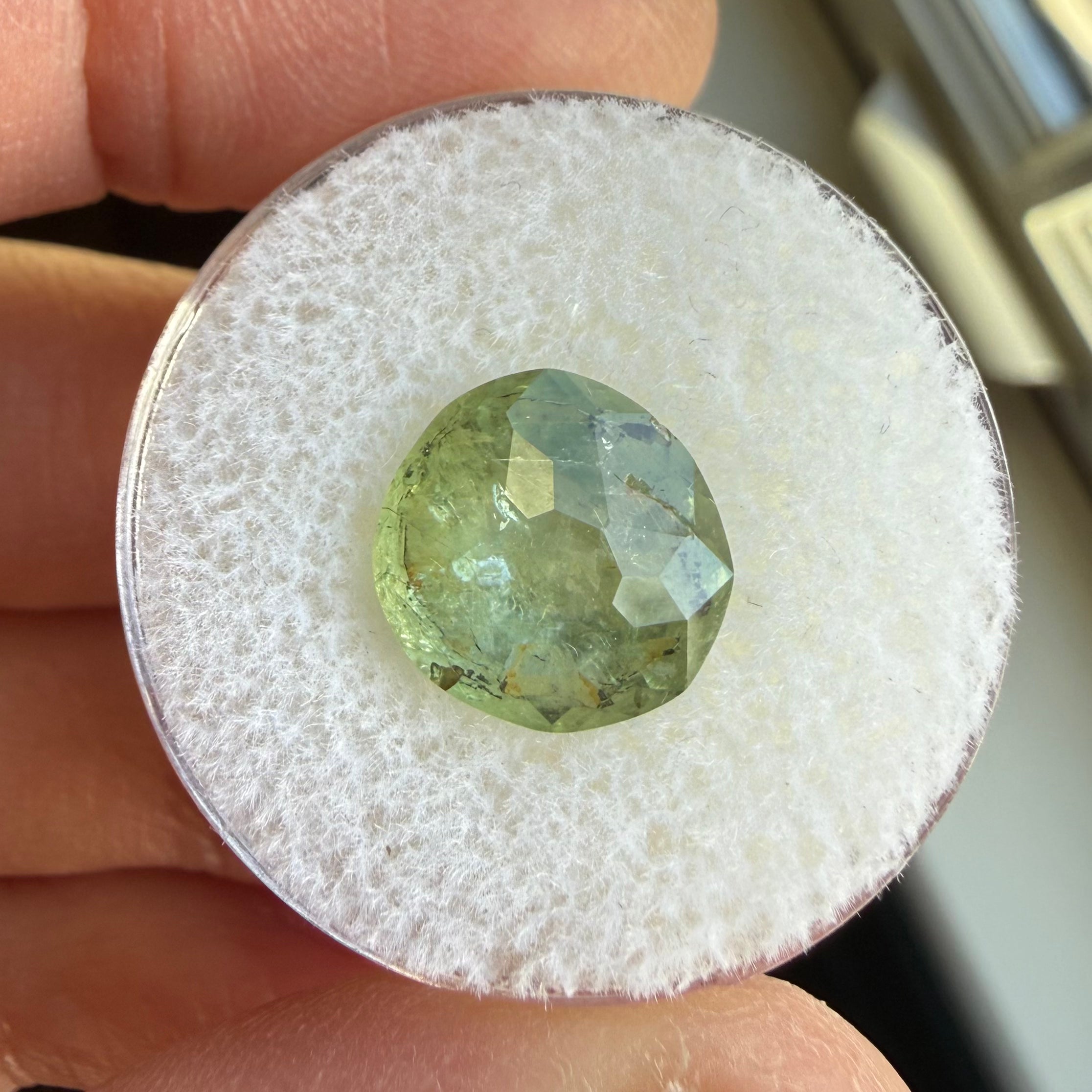Green gemstone on a white cushion held between fingers