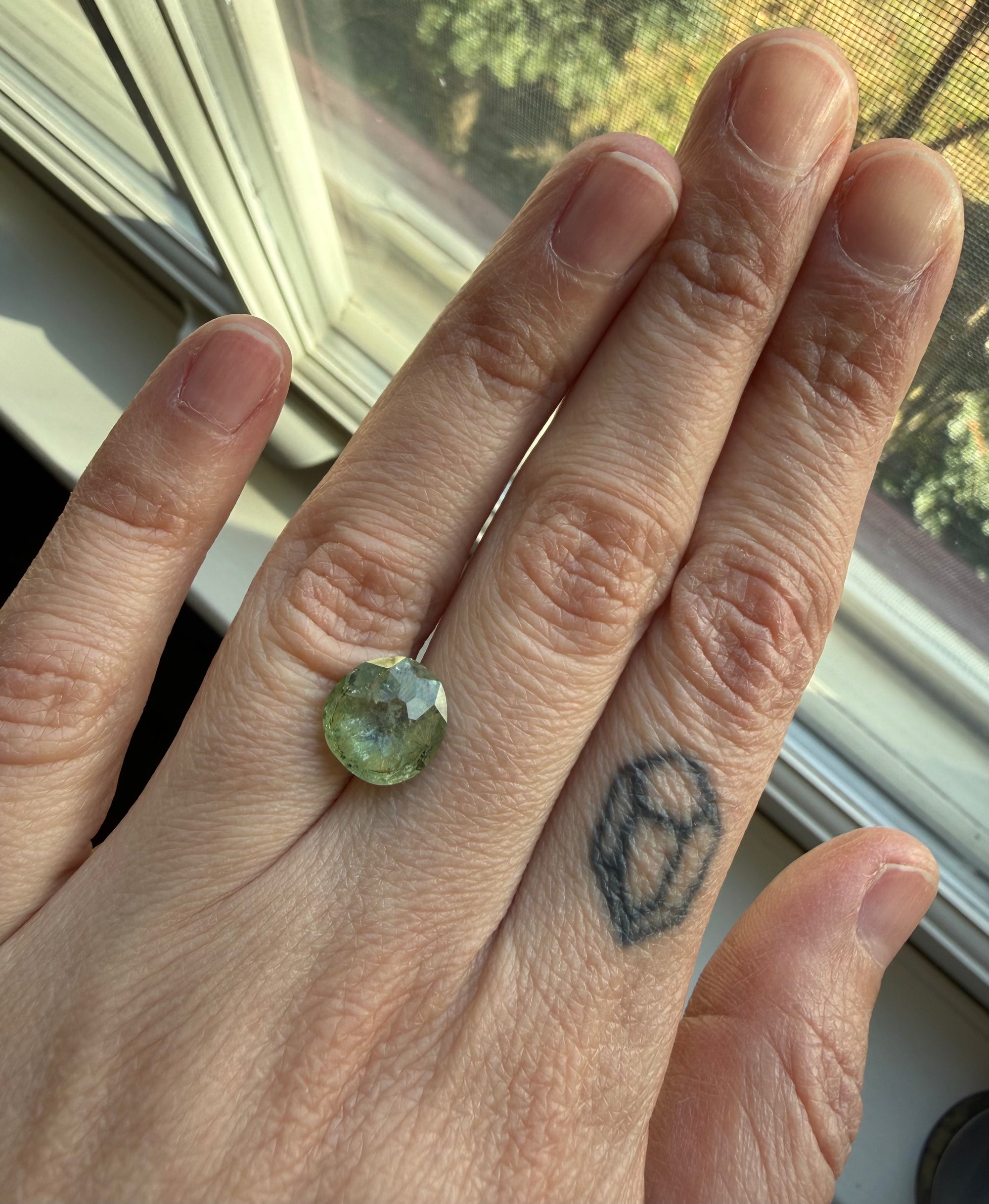 Hand wearing a green gemstone, tattoo visible.
