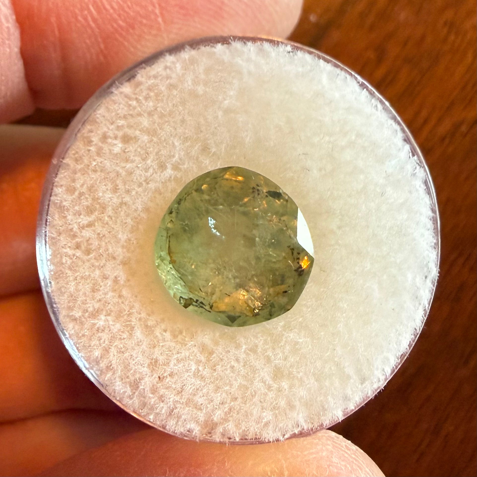 Green gemstone in a clear holder held by a hand on a wooden surface