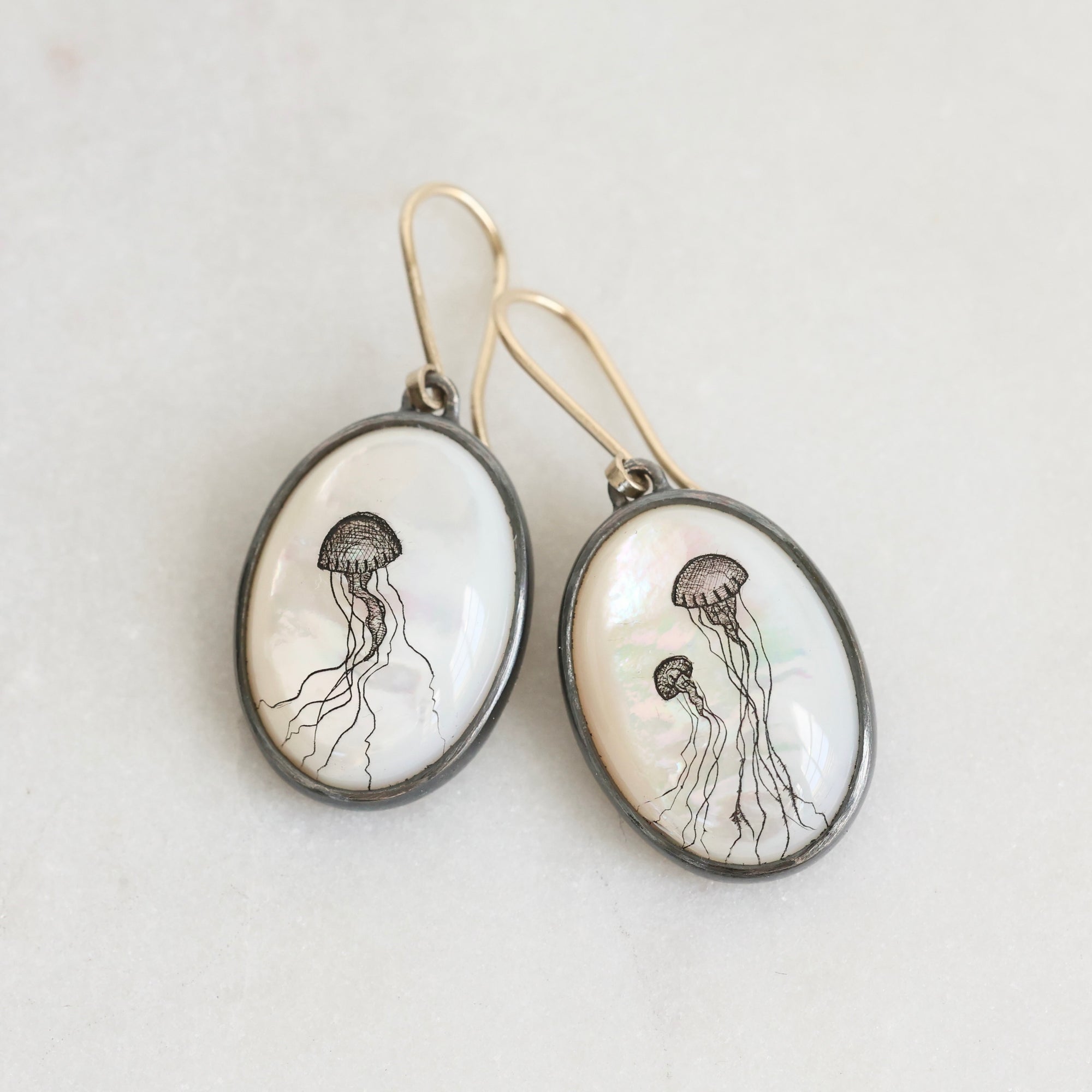 Oval-shaped earrings with jellyfish illustrations on a light background