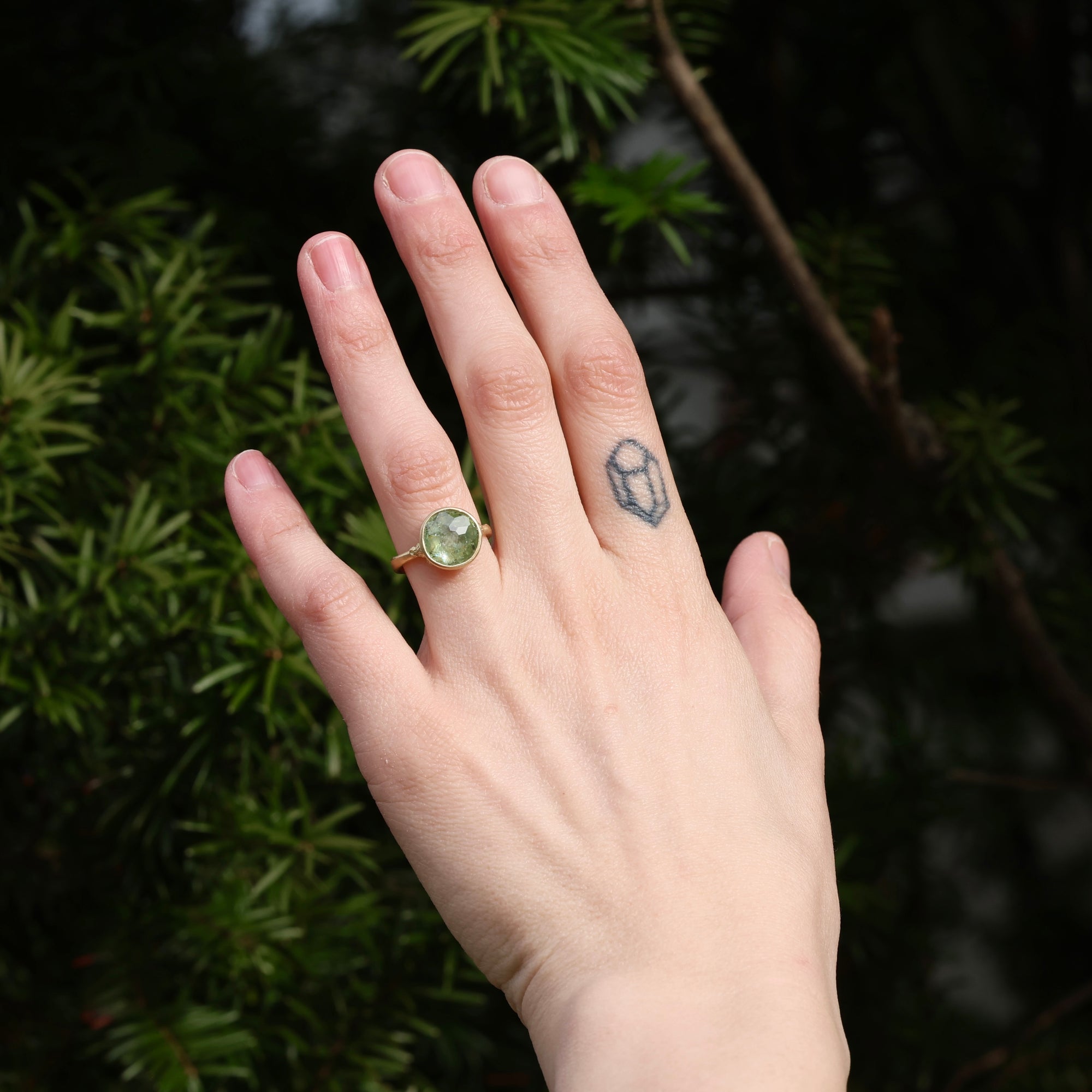 Hand wearing a green gemstone ring with a blurred natural background