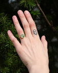 Hand wearing a green gemstone ring with a blurred natural background