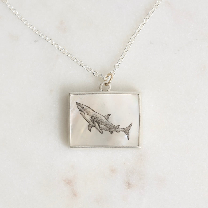 Silver necklace with a shark pendant on a marble surface