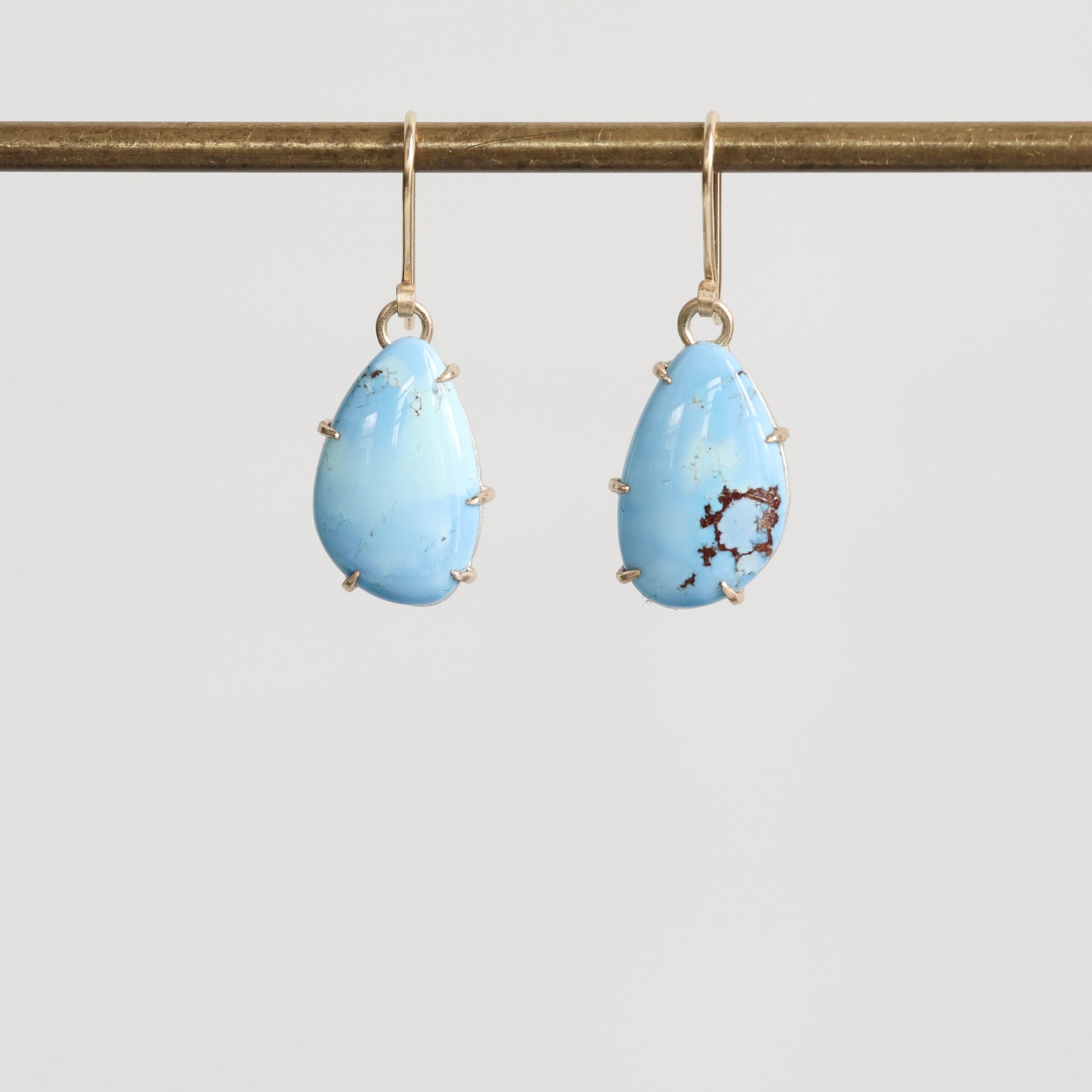 Pair of blue teardrop earrings on a gold earring stand against a light gray background