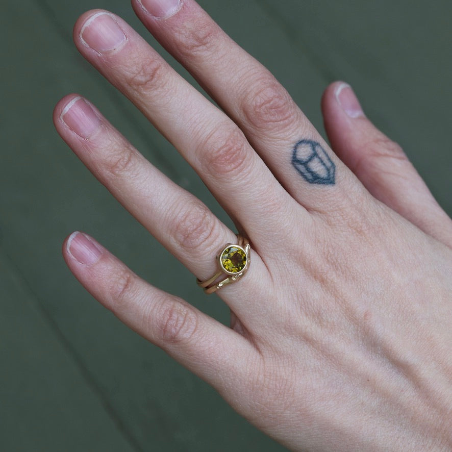 Hand wearing a gold ring with a green gemstone on a blurred background